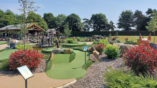 Mini golf course with vibrant greenery, playground equipment, and colorful shrubs under a clear blue sky.