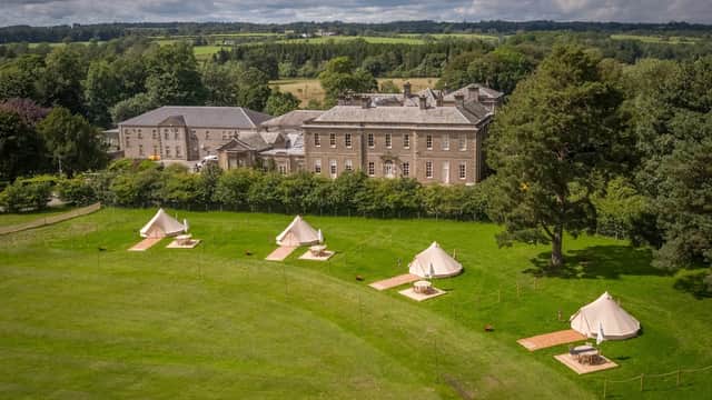 Gisburne Park Estate features a large historic building and glamping tents on a lush green lawn surrounded by trees.