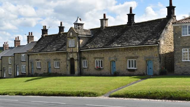Coxwold Village Hall features a stone faΓ§ade with a central entrance and a clock tower, surrounded by green grass.
