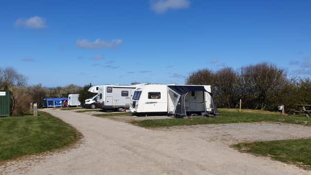 Caravans parked along a gravel path in a grassy area, with blue skies and scattered clouds in the background.
