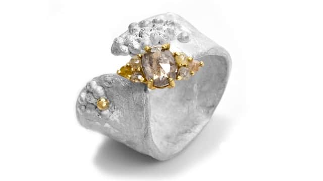 Unique silver ring with textured design and a central golden stone, showcasing a blend of elegance and artistry.