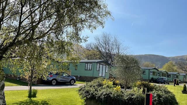 Lush green lawn with holiday caravans, trees, and a clear blue sky at Toft Hill Country Holiday Park in North Yorkshire.