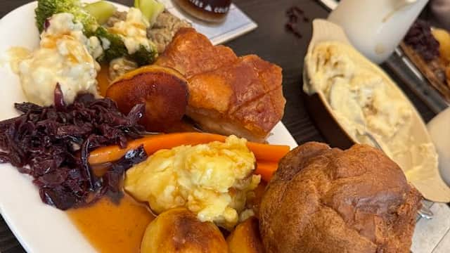 A plate of roast dinner featuring Yorkshire pudding, vegetables, and gravy, alongside drinks on a table.