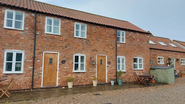 Charming brick cottages with wooden doors, potted plants, and outdoor seating in a tranquil rural setting.