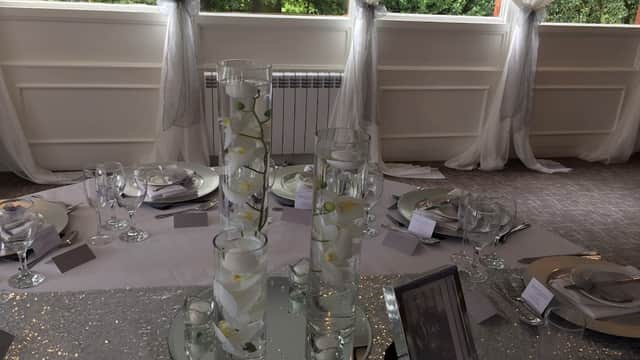 Elegant table setting with glass vases, white flowers, and silver accents, surrounded by sheer drapery.