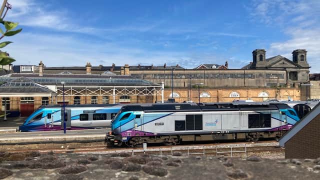 Two trains are stationed at Scarborough Railway Station, with a historic building and blue sky in the background.