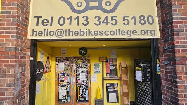 Bright yellow entrance with a large bike chain graphic, contact info, and various stickers on the door in Leeds.