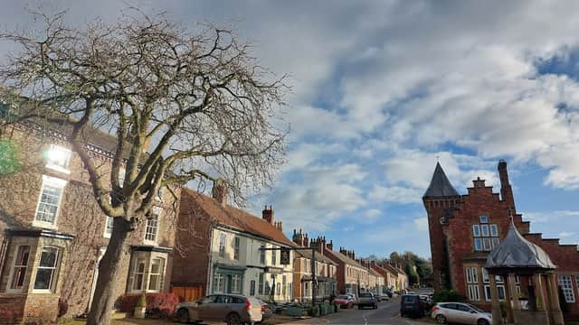 Helperby Village Hall with a tree, traditional houses, and a tower in a quaint Yorkshire village setting.