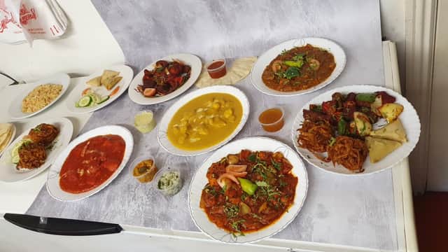 A variety of colorful dishes including curries, rice, and bread on white plates, arranged on a table.