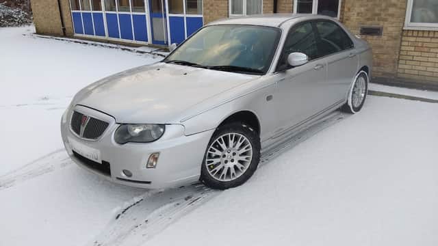 Silver car parked on snowy ground outside a brick building with windows in Little Weighton, Yorkshire.