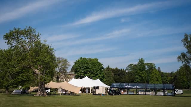 Large white and beige tents set up on green grass, surrounded by trees under a clear blue sky.