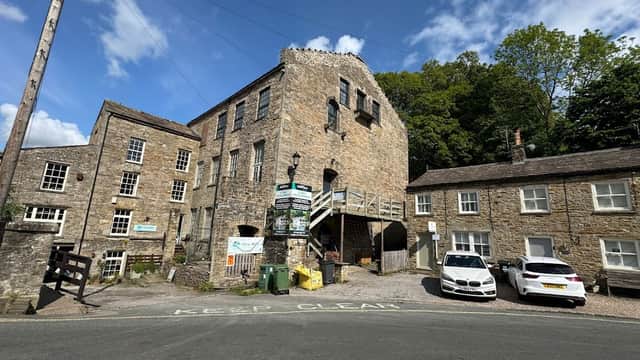 Historic stone building with multiple stories, surrounded by greenery and parked cars, near a road in West Burton.
