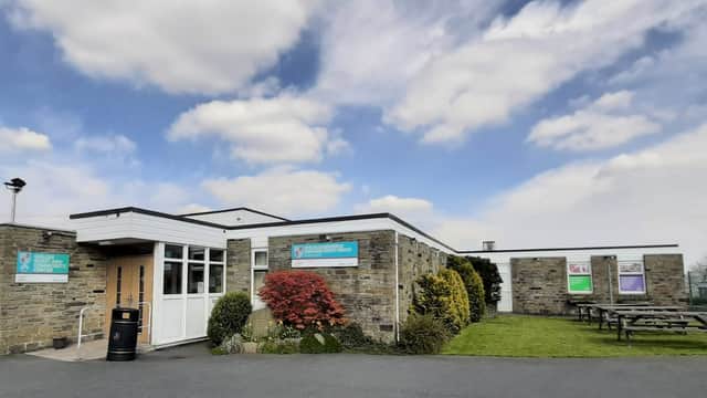 Modern stone building with large windows, green lawn, picnic tables, and a blue sky with scattered clouds.