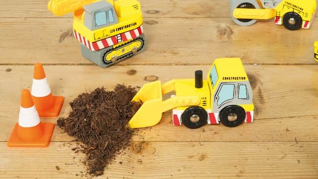 Toy construction vehicles, traffic cones, and a pile of dirt on a wooden surface.