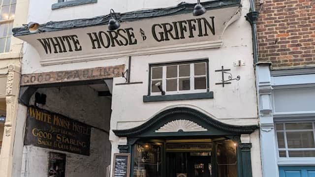 Historic building with a sign reading "White Horse & Griffin," featuring a welcoming entrance and cobblestone street.
