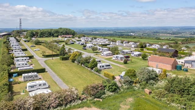 Expansive view of Wolds Way Caravan and Camping, featuring neatly arranged caravans and lush green fields under a blue sky.