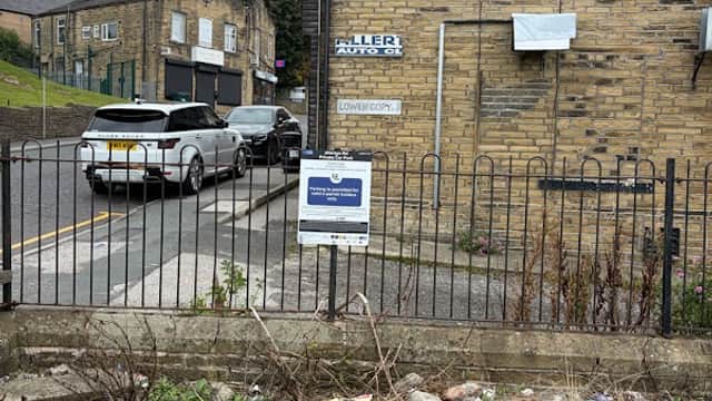 Private car park sign in Clayton, Yorkshire, with parked cars and a stone building in the background.