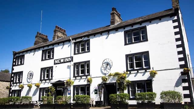 White building with black trim, large windows, flower boxes, and a sign reading "NEW INN" under a clear blue sky.