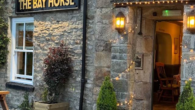 Stone exterior of The Bay Horse pub with warm lighting, wooden seating, and planters outside the entrance.