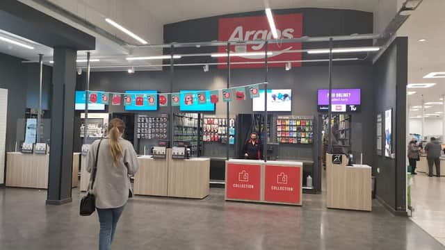 Interior of a retail space with an Argos collection counter, digital screens, and a customer browsing.