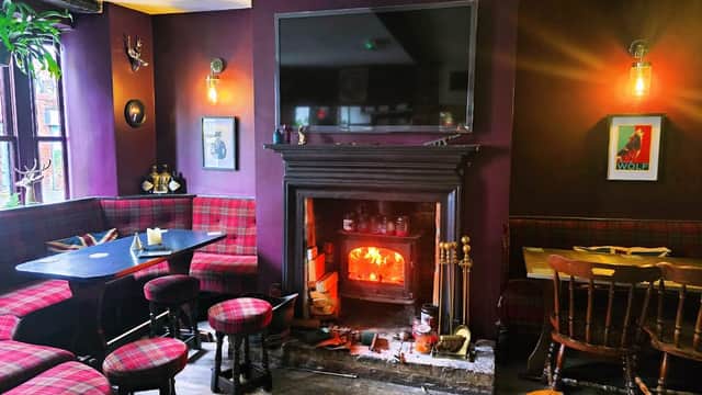 Cozy bar interior with plaid seating, a fireplace, and a large TV on a purple wall, creating a warm atmosphere.