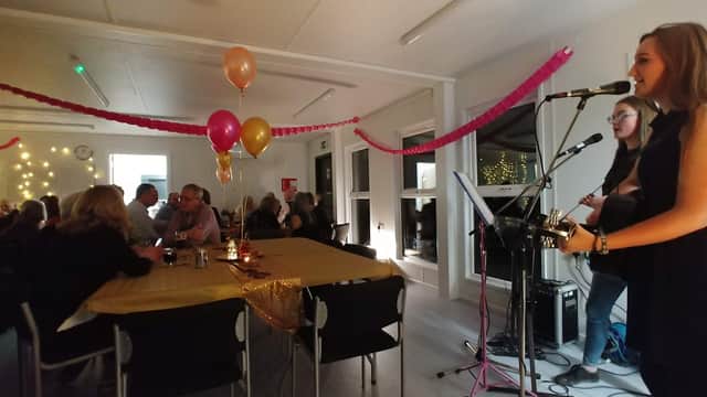 A lively event in Croft Village Hall with musicians, balloons, and guests enjoying a festive atmosphere.