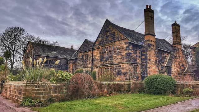 Historic stone building surrounded by lush greenery and garden features under a cloudy sky.