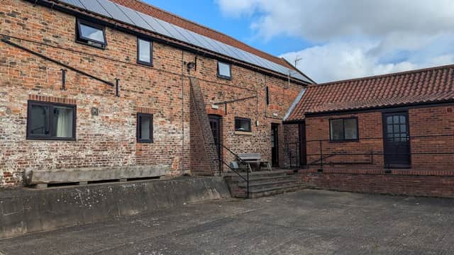 Brick buildings with solar panels, a staircase, and a courtyard under a blue sky with clouds at Highfield Farm Campsite.