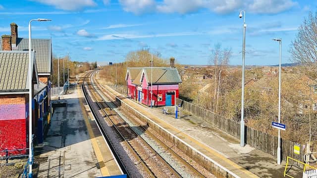 Two red railway buildings alongside empty platforms and tracks under a blue sky with scattered clouds.