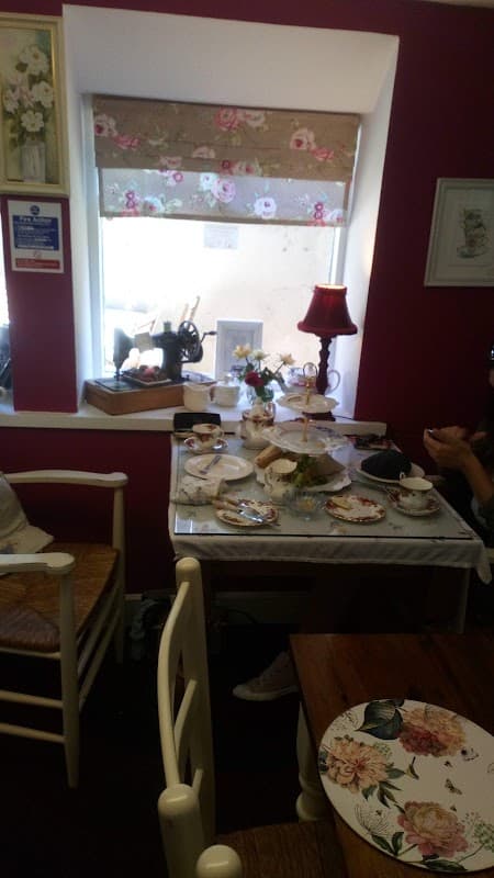 A cozy homeware shop with vintage tableware, a sewing machine, and floral decor, featuring a window with soft light.