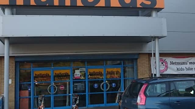Halfords store entrance with large orange signage, blue doors, and a parked car in front.