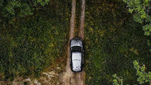 Aerial view of a black car parked on a dirt track surrounded by lush greenery in Coniston Off-Road Centre.