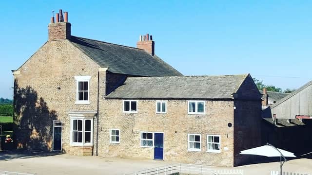 Charming brick farmhouse with multiple chimneys, white windows, and a blue door, set against a clear blue sky.