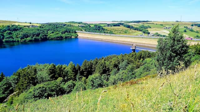 Scammonden Water with a blue sky, green hills, and a dam in the distance, surrounded by lush vegetation.