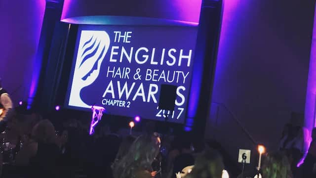 The English Hair & Beauty Awards 2017 displayed on a large screen, with a dimly lit venue and elegantly dressed attendees.
