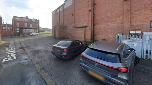 Two parked cars beside a brick wall and a gated area, with a street sign visible in the foreground.