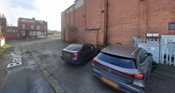 Two parked cars beside a brick wall and a gated area, with a street sign visible in the foreground.