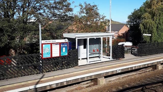 Bus stop at Pontefract Tanshelf with a clear blue sky, trees, and a nearby fence along the railway tracks.