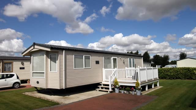 Caravan with a deck and potted plants, set against a blue sky with fluffy clouds at Four Acres Caravan Park.