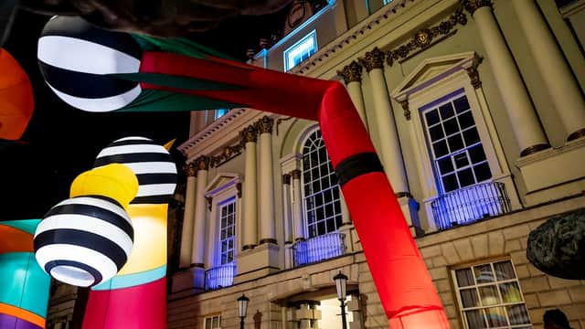 Colorful large balloons and structures in front of a historic building, illuminated at night with vibrant lights.