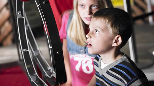 Children engaged with a rolling ball exhibit at a museum, displaying curiosity and focus in a brightly lit space.