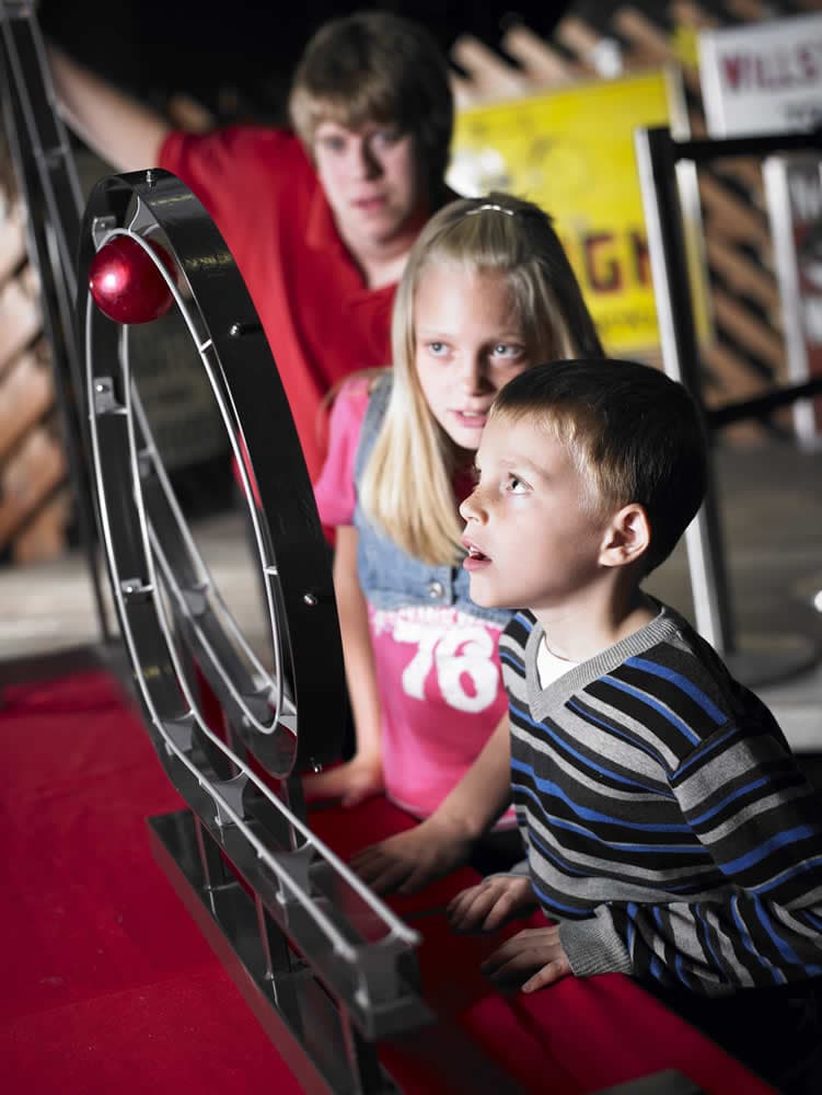Children engaged with a rolling ball exhibit at a museum, displaying curiosity and focus in a brightly lit space.