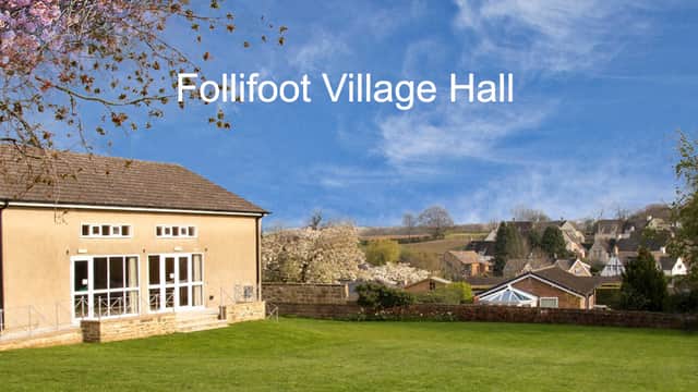 Follifoot Village Hall surrounded by greenery and houses, under a clear blue sky with blooming trees.