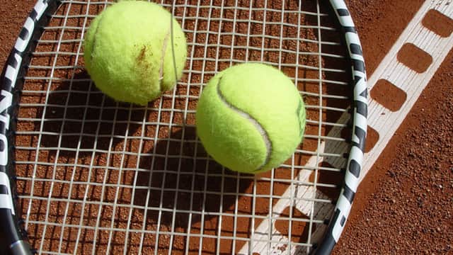 Two bright yellow tennis balls resting on a tennis racket, placed on a clay court with white lines.