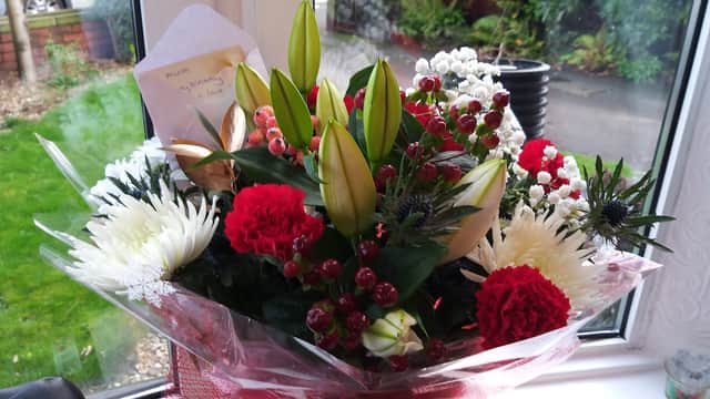 Colorful floral bouquet featuring red and white flowers, green leaves, and decorative elements in a window setting.