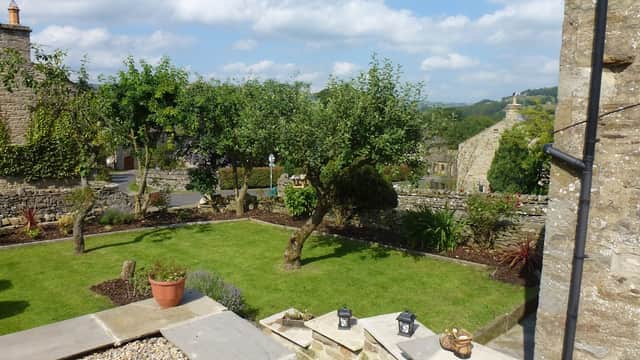 Quaint garden with trees, stone walls, and a clear blue sky in West Burton, Yorkshire, near Flag Cottage.