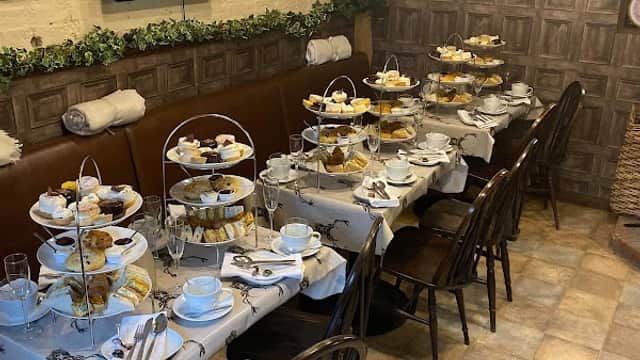 A cozy bakery setting with tables set for afternoon tea, featuring tiered stands of pastries and decorative wall art.