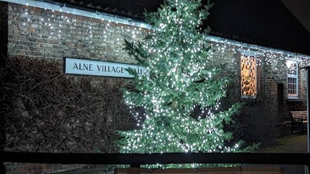 Alne Village Hall illuminated at night with a decorated Christmas tree and a banner for a pop-up pub event.