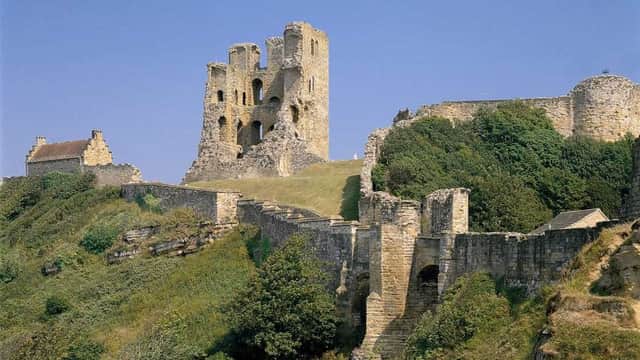 Ruins of Scarborough Castle stand against a blue sky, overlooking the sea and green landscape.