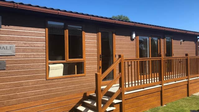 Wooden lodge with a patio and steps, set against a clear blue sky and green grass in Cliffe Common, Yorkshire.